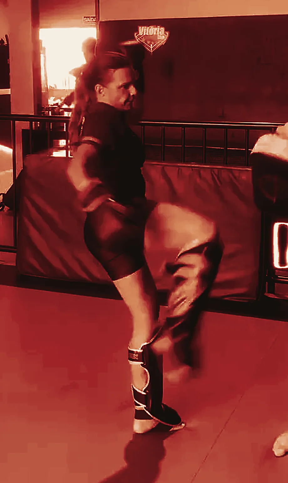 Daniela de luvas e caneleiras, em movimento de chute durante um treino de Muay Thai