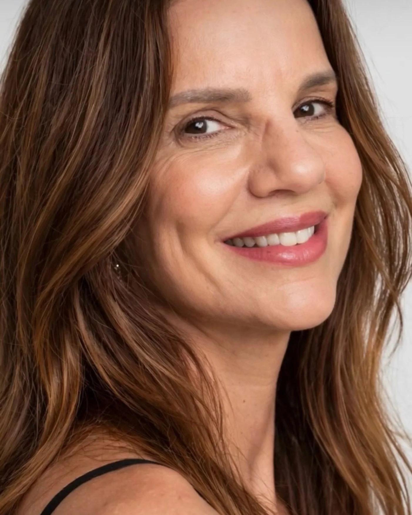 Daniela Barreto sorrindo, olhando por cima do ombro, em retrato de estúdio